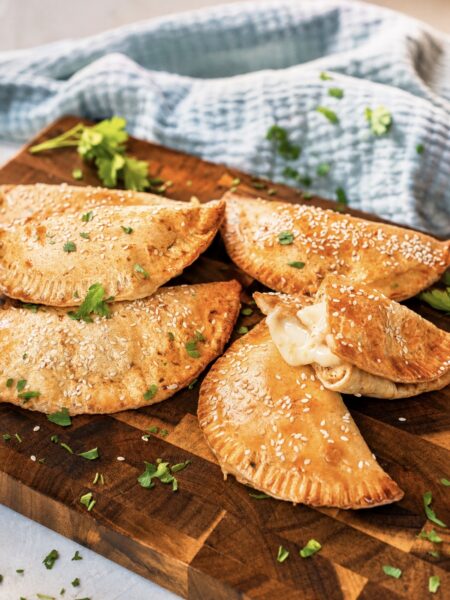 Cheesy Chicken Tortilla Pockets served on a wooden board, with one pocket broken apart to reveal the chicken and mozzarella filling.