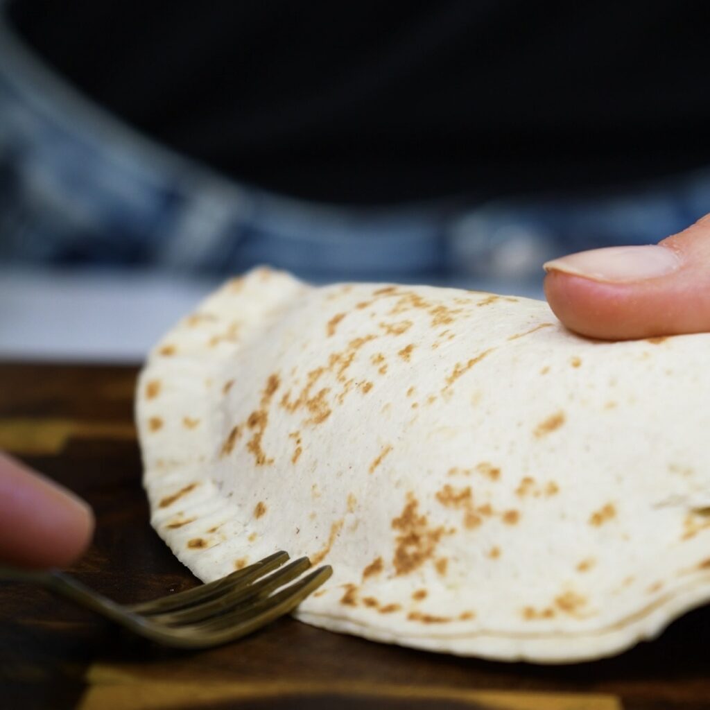 Crimping the edges of a filled tortilla pocket with a fork to seal it.