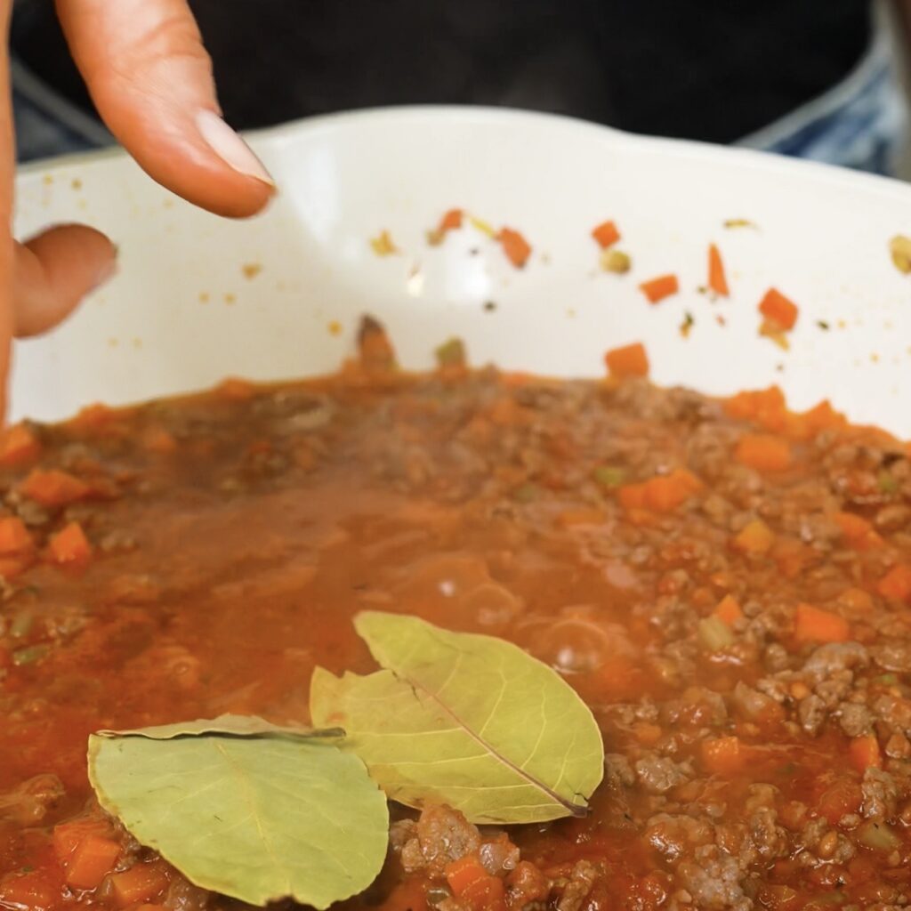 Bay leaves being added to a pan of beef ragù.