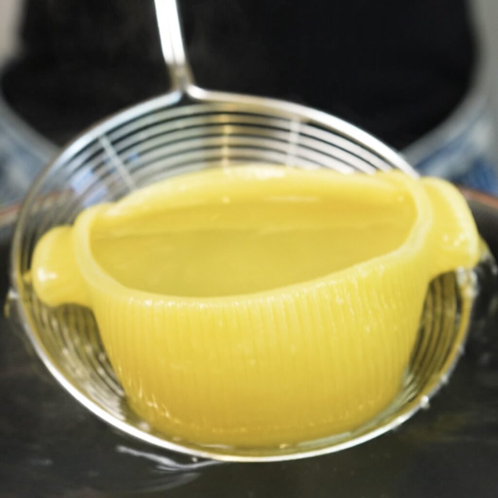Cooked Caccavelle pasta shell being carefully lifted from a saucepan of boiling water.