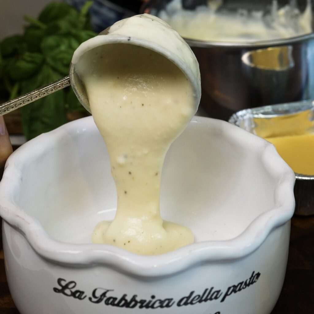 Béchamel sauce being poured into the bottom of a baking dish.
