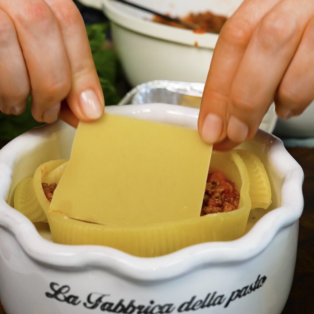 Mini lasagna sheets being layered with beef ragù inside a cooked Caccavelle pasta shell.