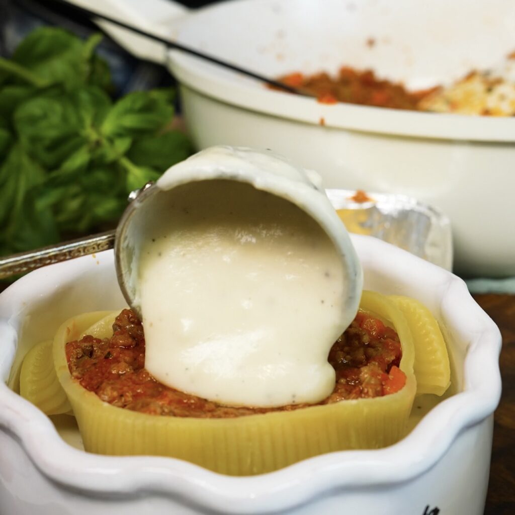 Béchamel sauce being spooned over the final layer of beef ragù and lasagna inside the Caccavelle pasta shells.
