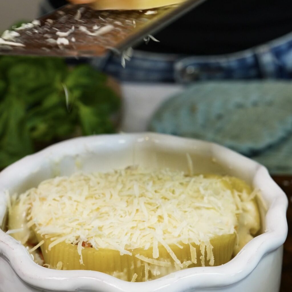 Grated Parmesan being sprinkled over the béchamel-topped Caccavelle pasta shells before baking.