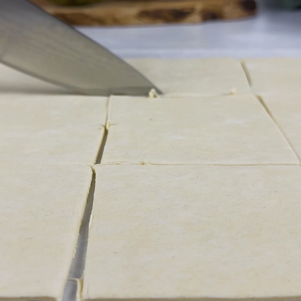 Cutting a sheet of puff pastry into equal squares for Pesto Mozzarella Puffs.