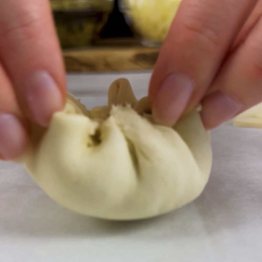 Sealing a filled puff pastry square and shaping it into a small ball.