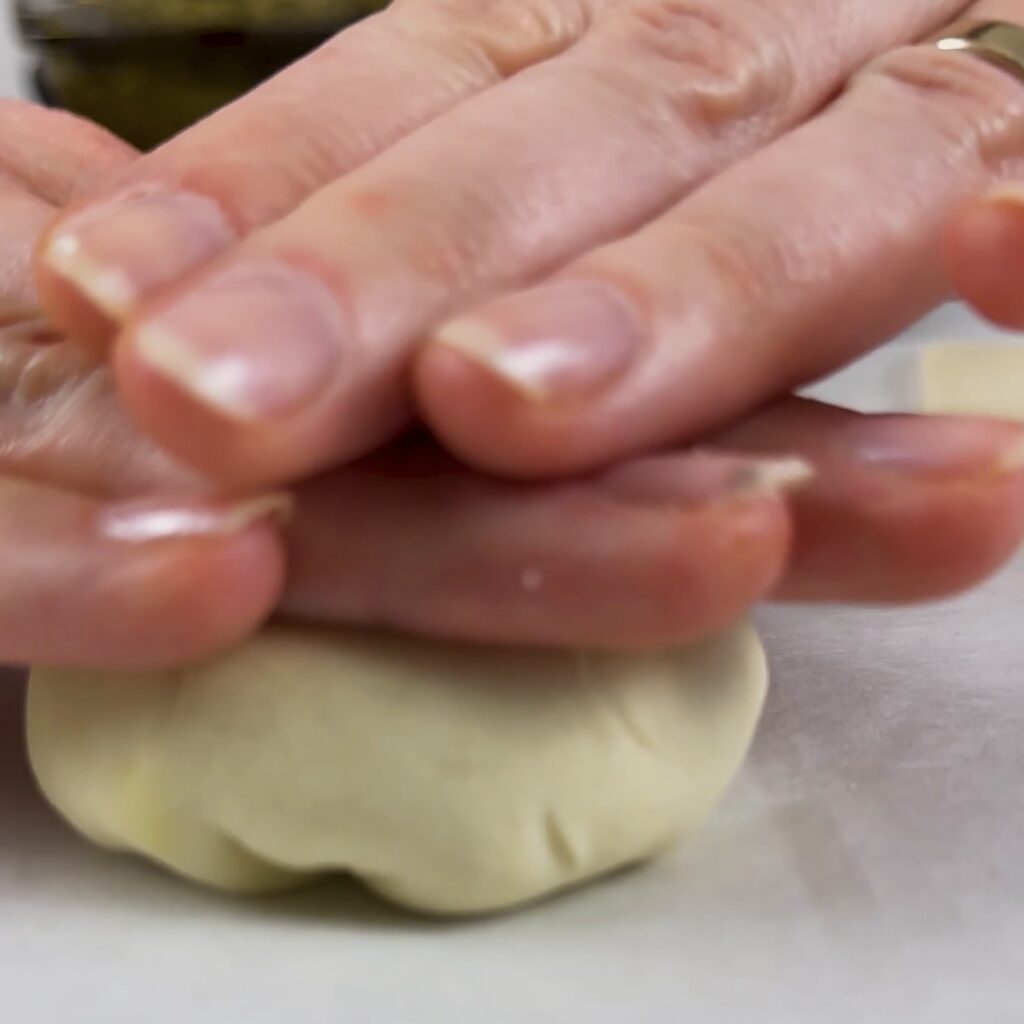 Gently flattening a filled puff pastry ball with the palm of a hand.