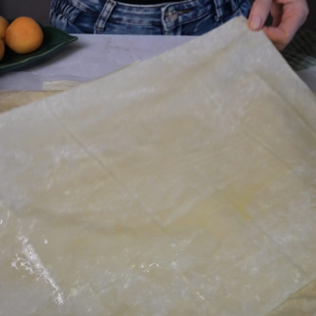 Layering filo pastry sheets at different angles and brushing each layer with melted butter for the Cottage Cheese Apricot Galette