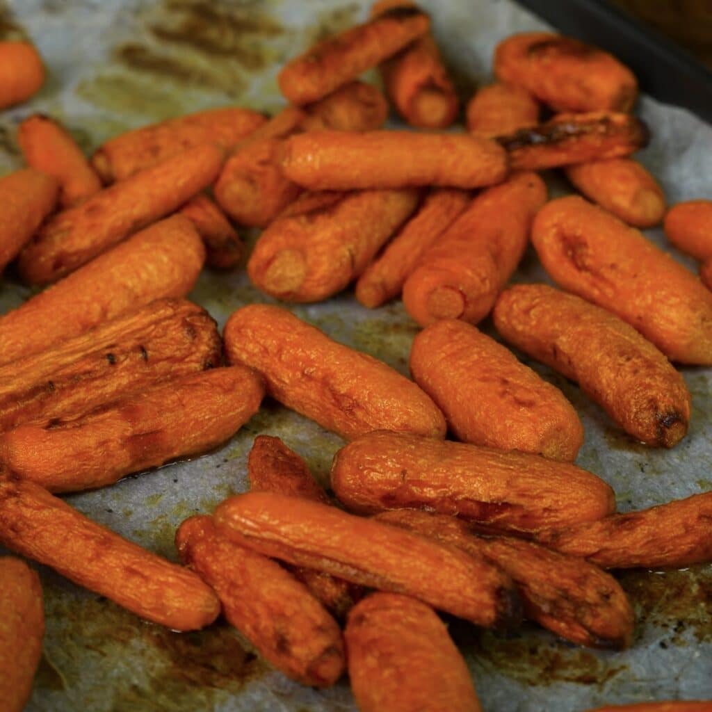 Honey-roasted baby carrots golden and caramelised on a lined baking tray.