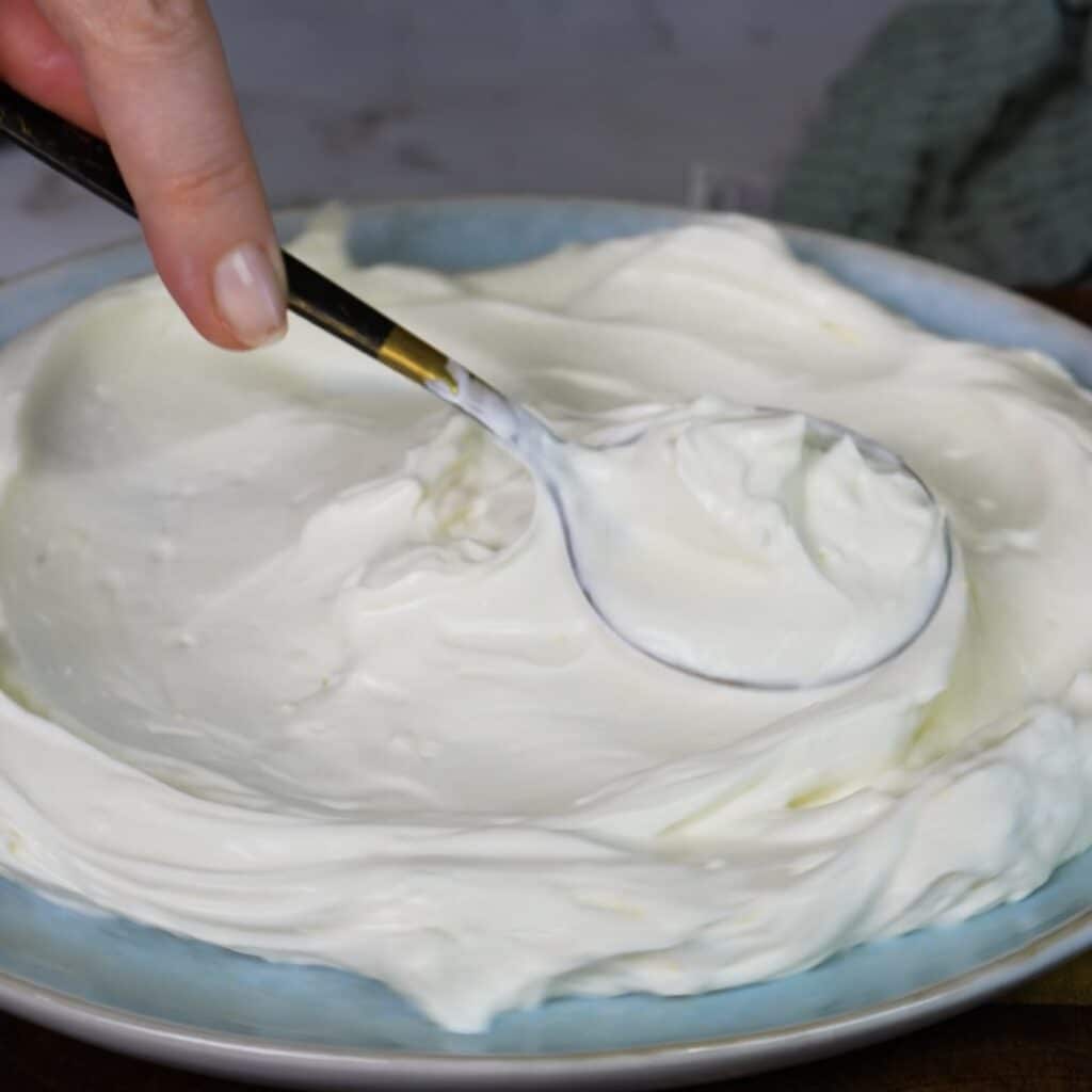 Creamy whipped feta being spread over a serving platter with the back of a spoon.