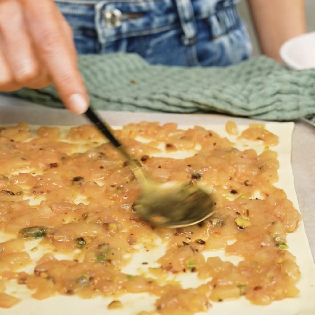 Spreading the peach and pistachio filling over puff pastry for Sticky Peach and Pistachio Buns.