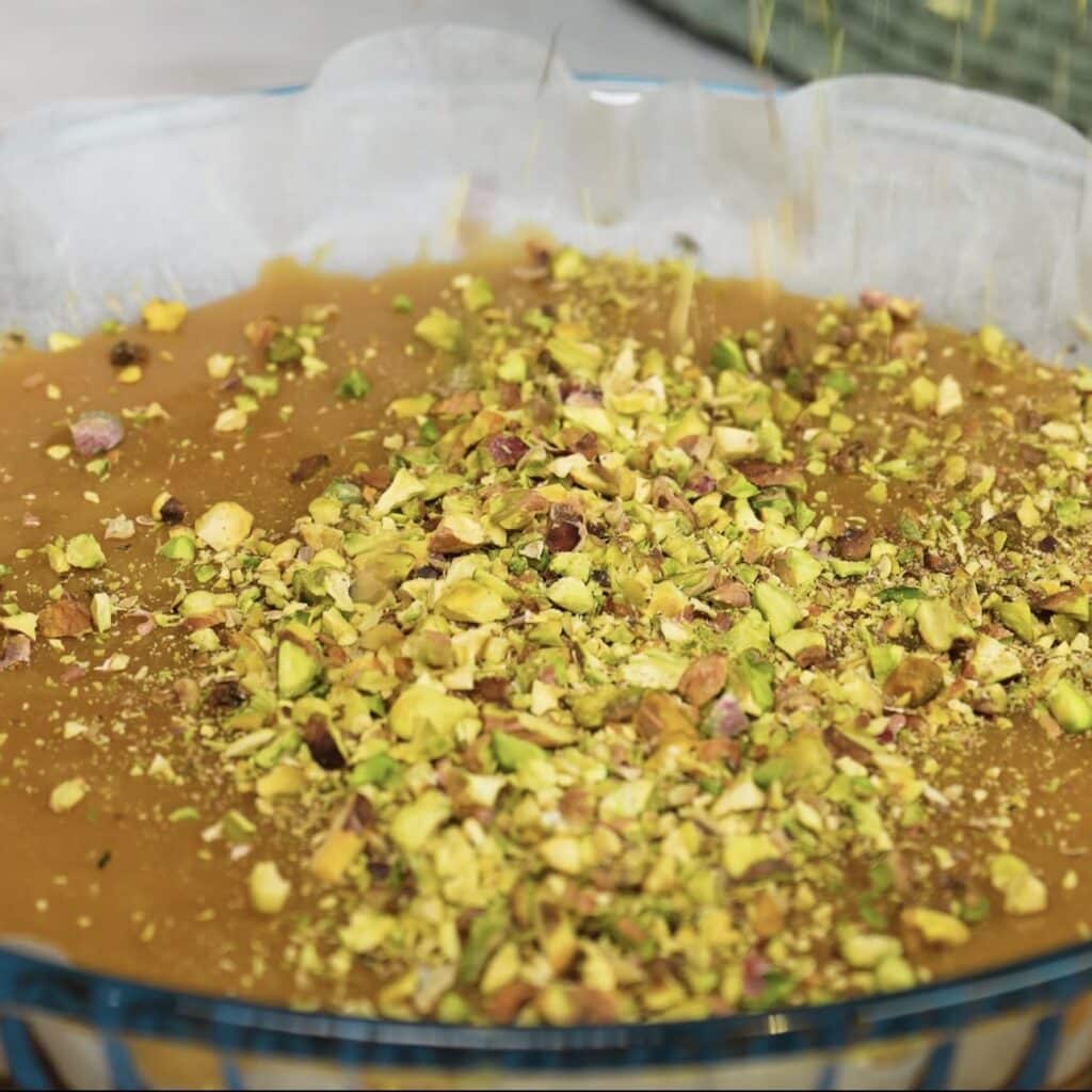 Sprinkling crushed pistachios over the caramel for Sticky Peach and Pistachio Buns.