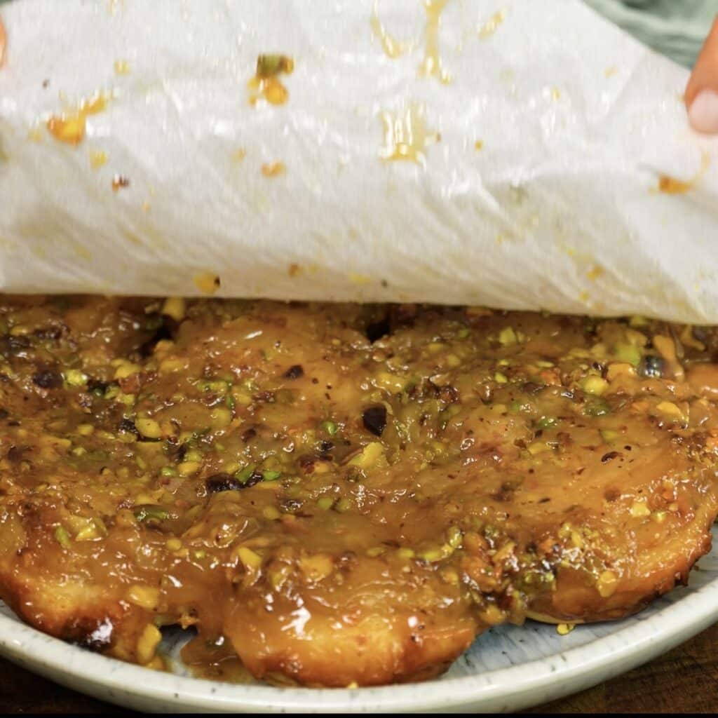 Peeling the parchment paper from freshly inverted Sticky Peach and Pistachio Buns.