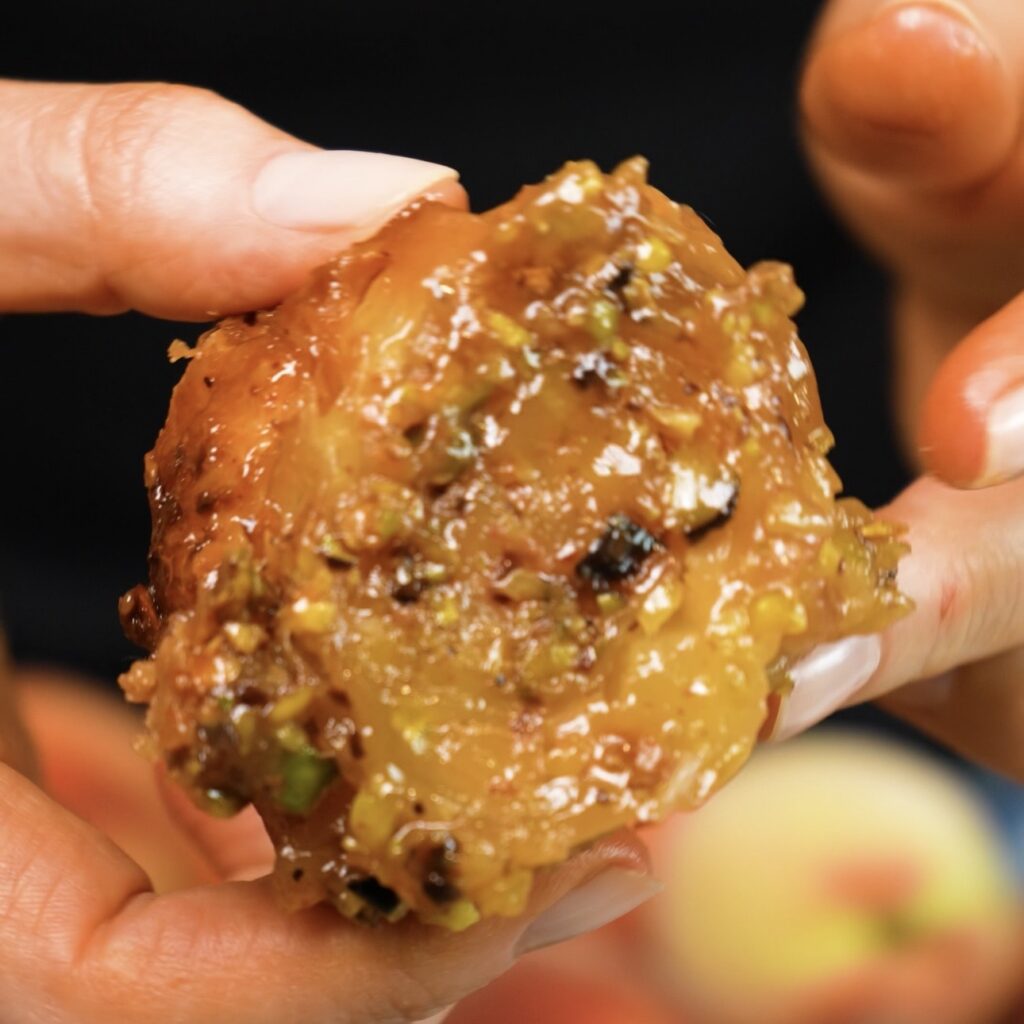 Hands holding one Sticky Peach and Pistachio Bun with a glossy caramel and pistachio topping.
