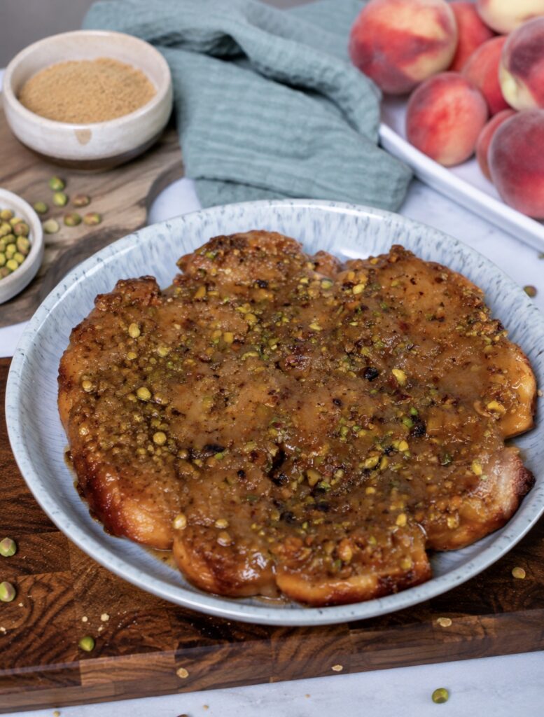 Sticky Peach and Pistachio Buns served on a plate with a glossy caramel and pistachio topping.