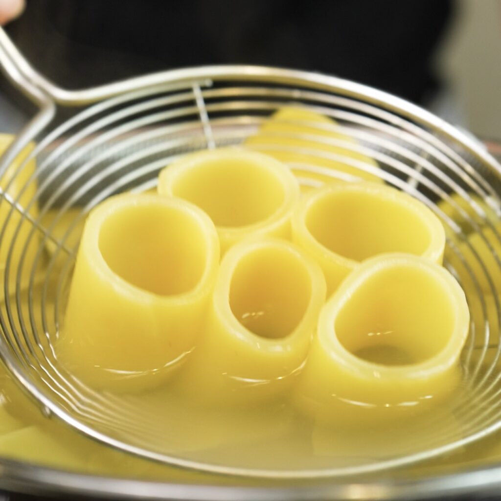 Taking cooked paccheri pasta out of the pot.