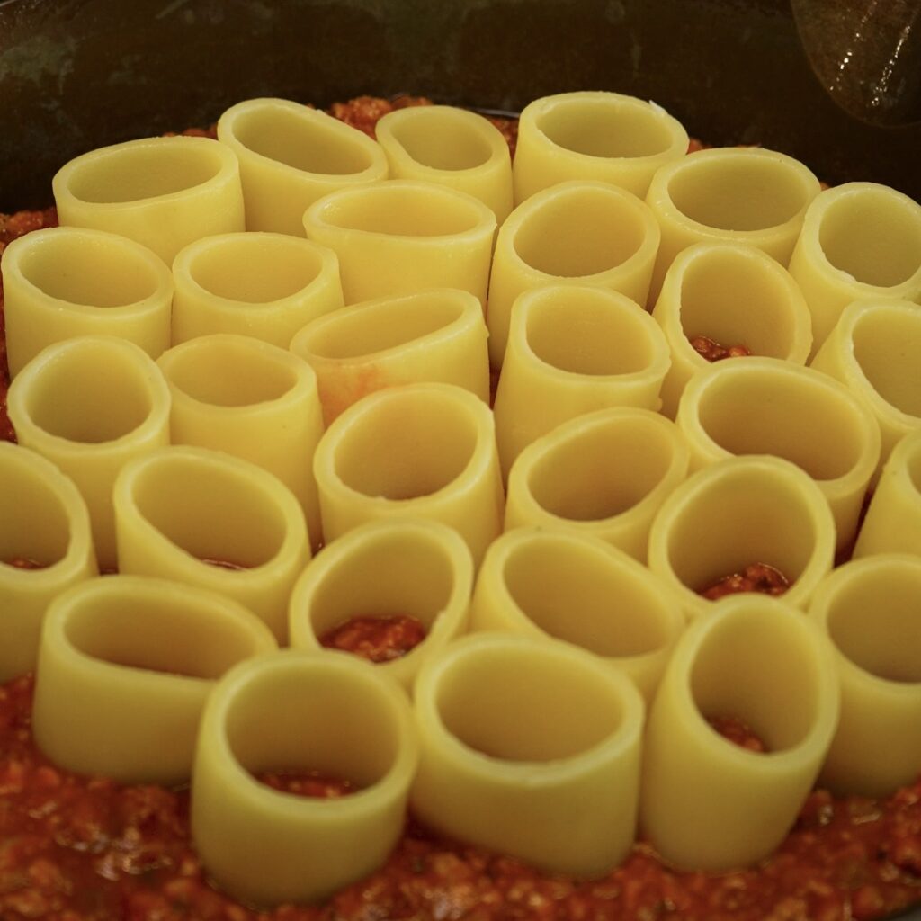 Arranging paccheri upright over a layer of Beef Ragù.