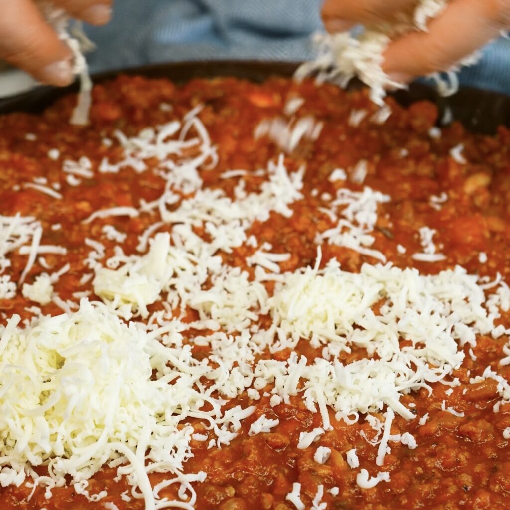 Sprinkling grated mozzarella over the top layer of Beef Ragù.