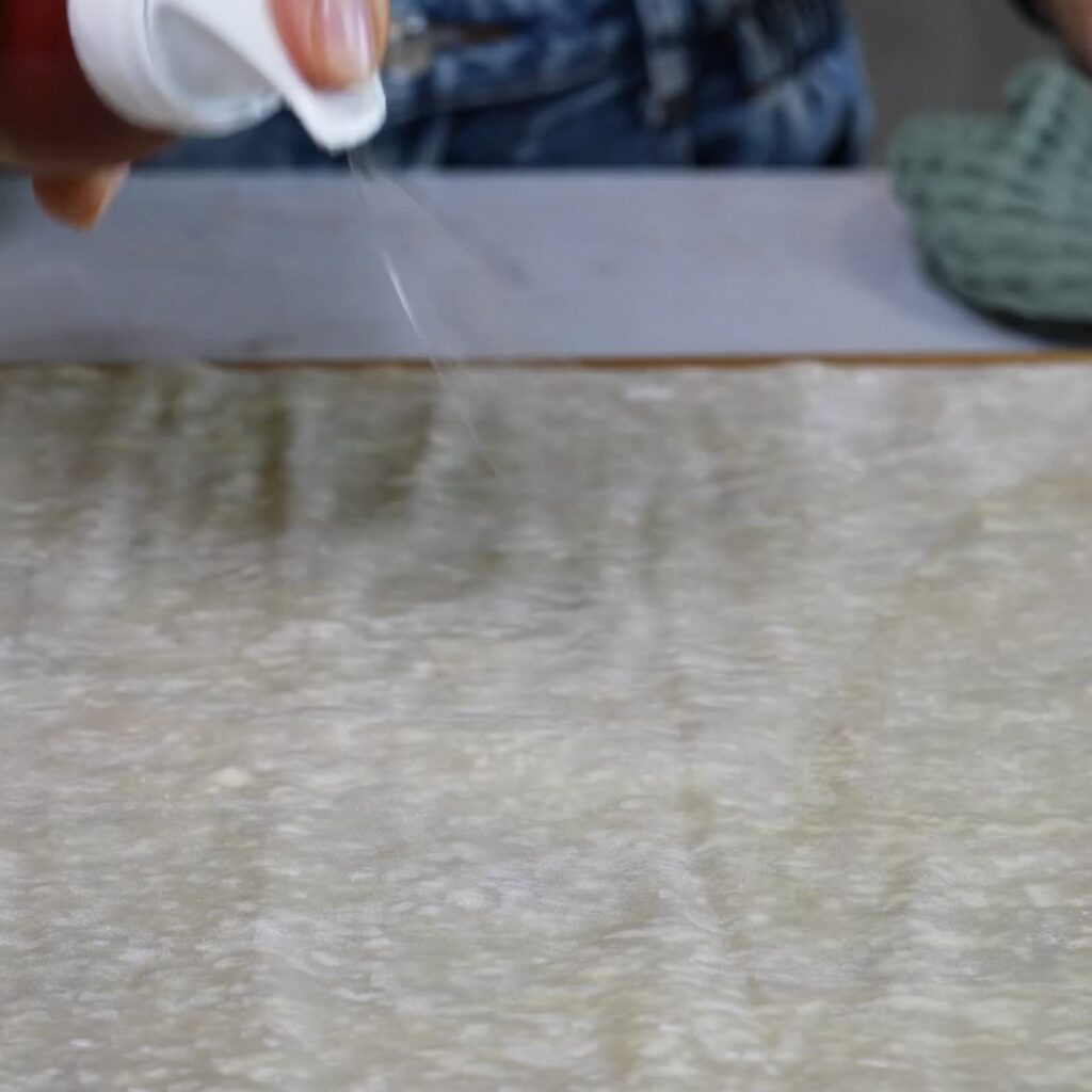 Spraying a filo pastry sheet with olive oil before adding the filling