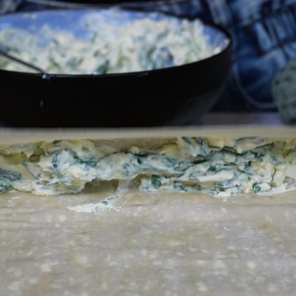 Rolling the filo pastry over the feta and spinach filling before adding the chopstick