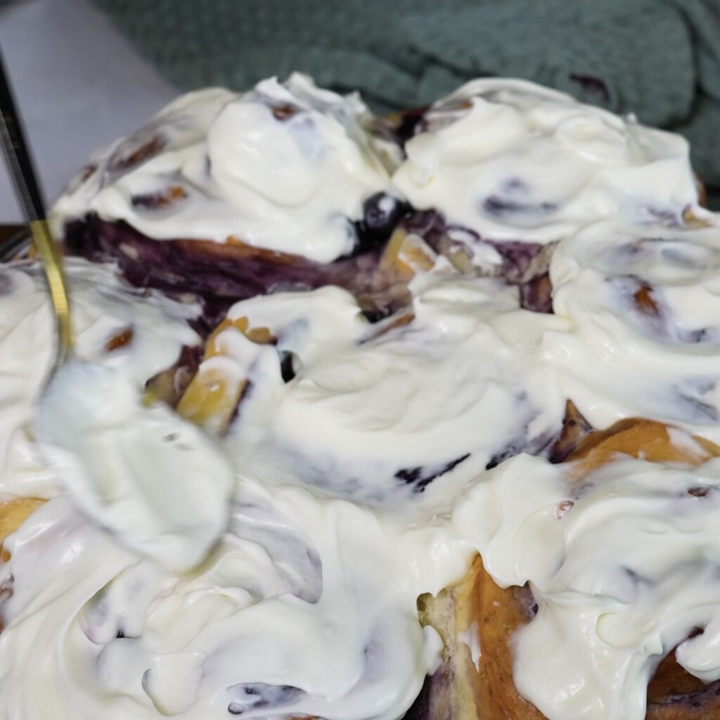 Adding cream cheese frosting to blueberry rolls
