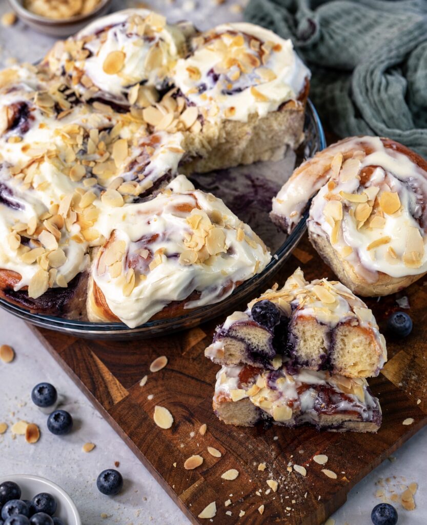 Blueberry Rolls in a baking dish with one sliced in half on a wooden board