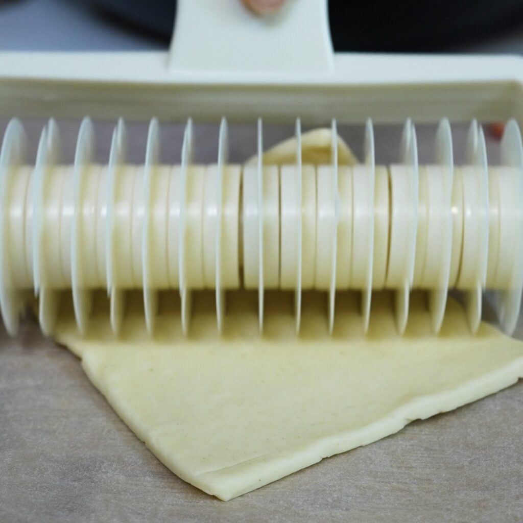 Cutting a puff pastry square with a lattice pastry cutter.