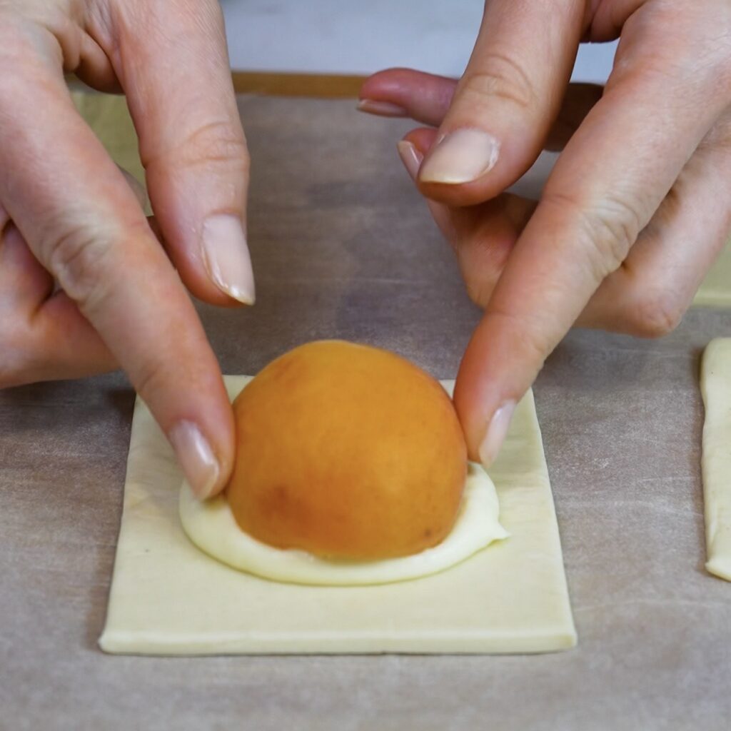 Apricot half placed on mascarpone filling in the centre of a solid puff pastry square.