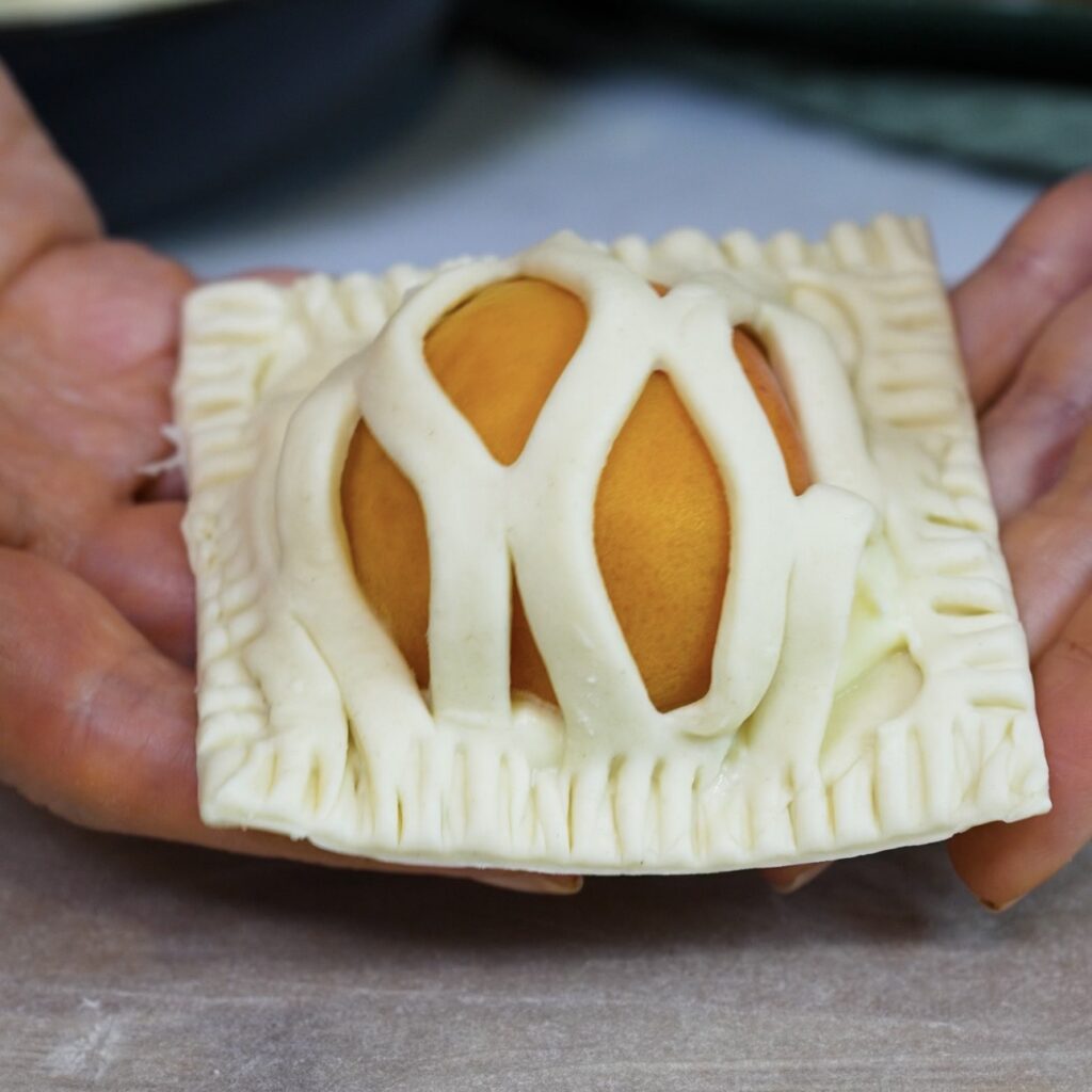 Hands holding an Apricot Mascarpone Puff with neatly trimmed edges before baking.