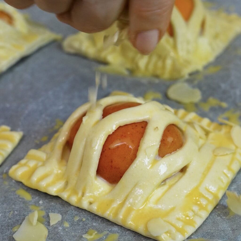 Apricot Mascarpone Puffs brushed with egg wash and sprinkled with almond flakes before baking.