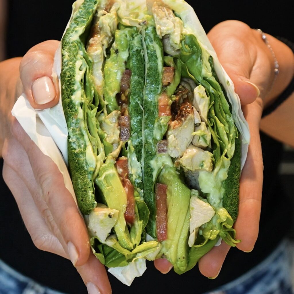Hands holding sliced High-Protein Spinach Sandwich to reveal the chicken and avocado filling