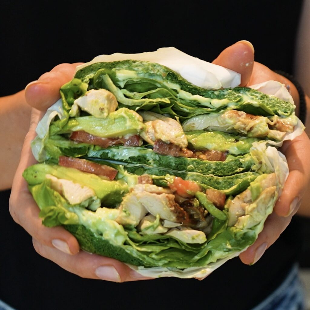Hands holding sliced High-Protein Spinach Sandwich to reveal the chicken and avocado filling