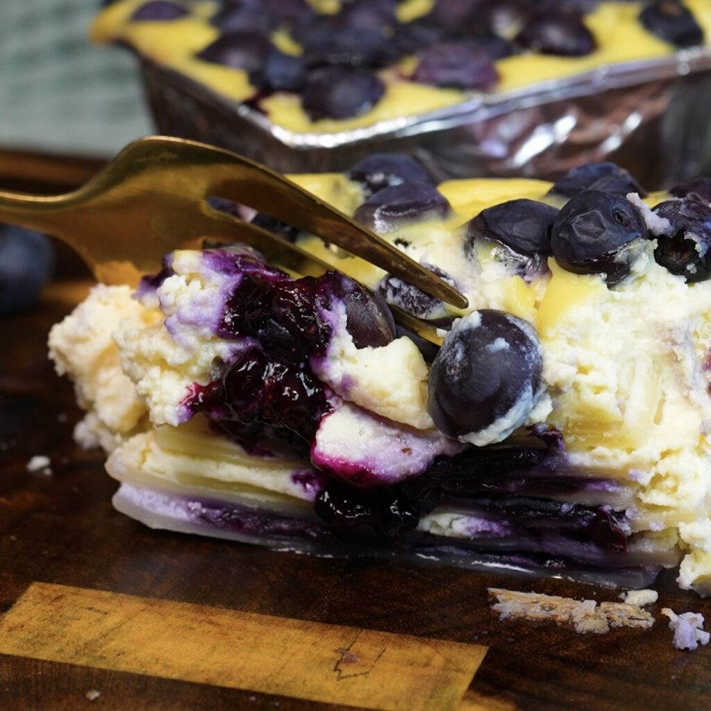 Fork breaking into Blueberry Ricotta Lasagna sliced in half to reveal the creamy blueberry and pasta layers.
