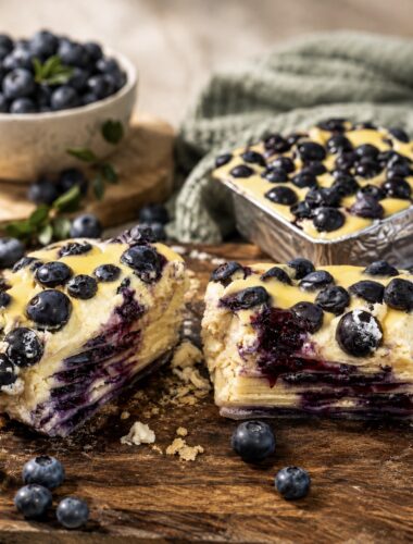 Blueberry Ricotta Lasagna served on a wooden board, sliced in half to show the creamy ricotta, blueberry and pasta layers.