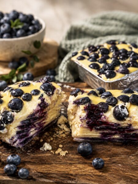 Blueberry Ricotta Lasagna served on a wooden board, sliced in half to show the creamy ricotta, blueberry and pasta layers.