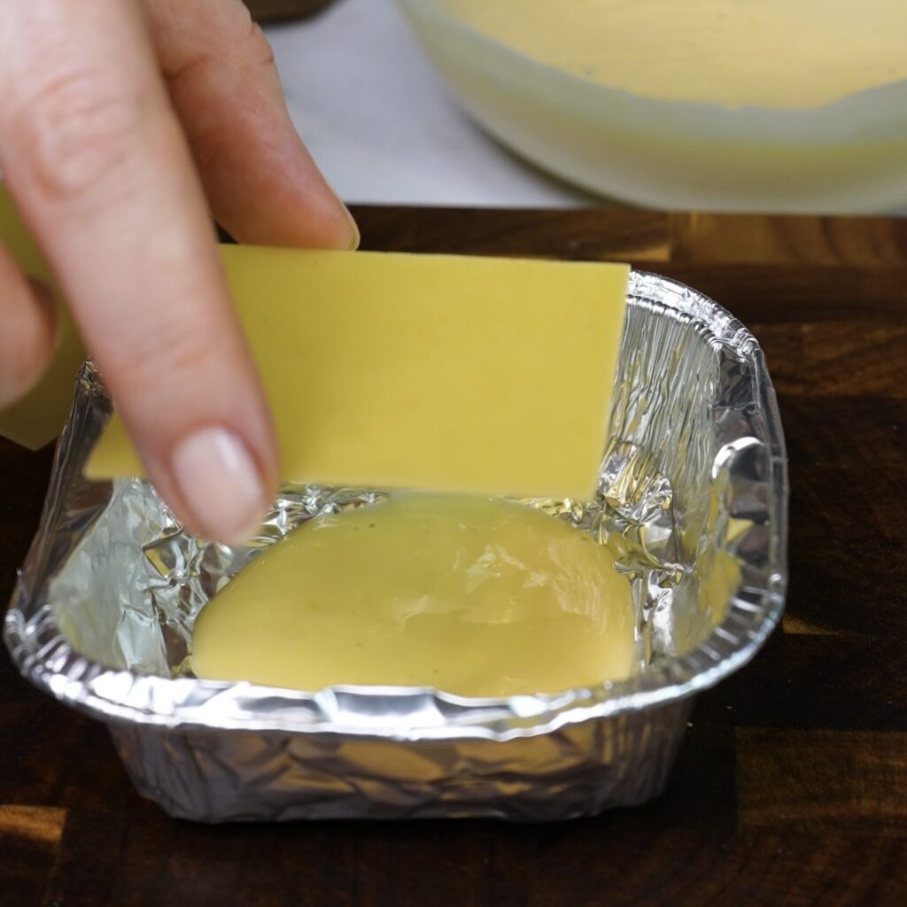 Adding the first layer of ricotta cream and a mini lasagna sheet to the baking container.
