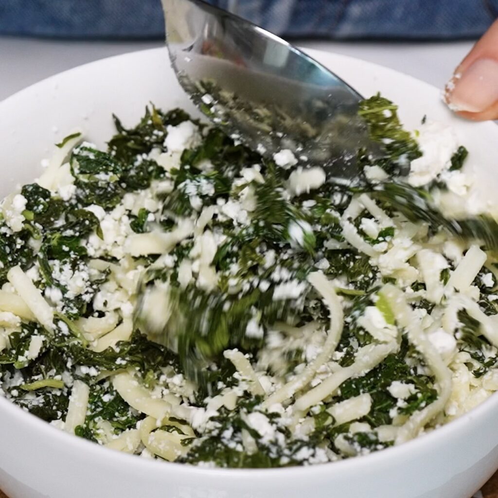 Spinach, crumbled feta and shredded mozzarella being mixed together in a bowl for Spinach Feta Rice Paper Bombs.