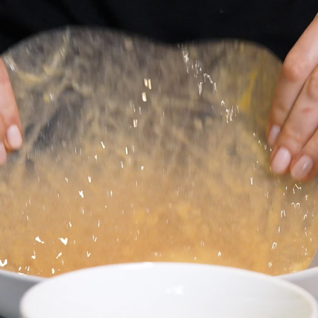 Rice paper sheet being dipped into an egg and milk mixture for Spinach Feta Rice Paper Bombs.