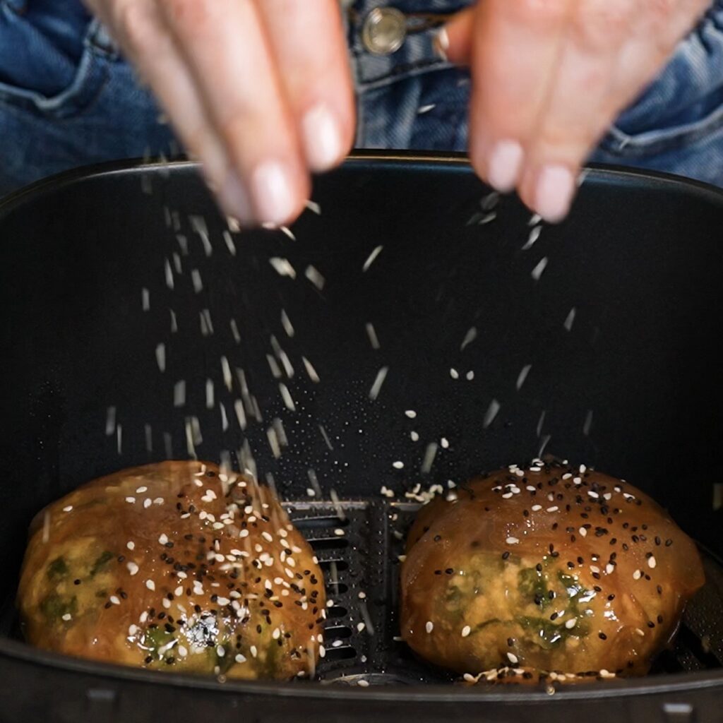 Sprinkling sesame seeds over Spinach Feta Rice Paper Bombs in the air fryer basket.