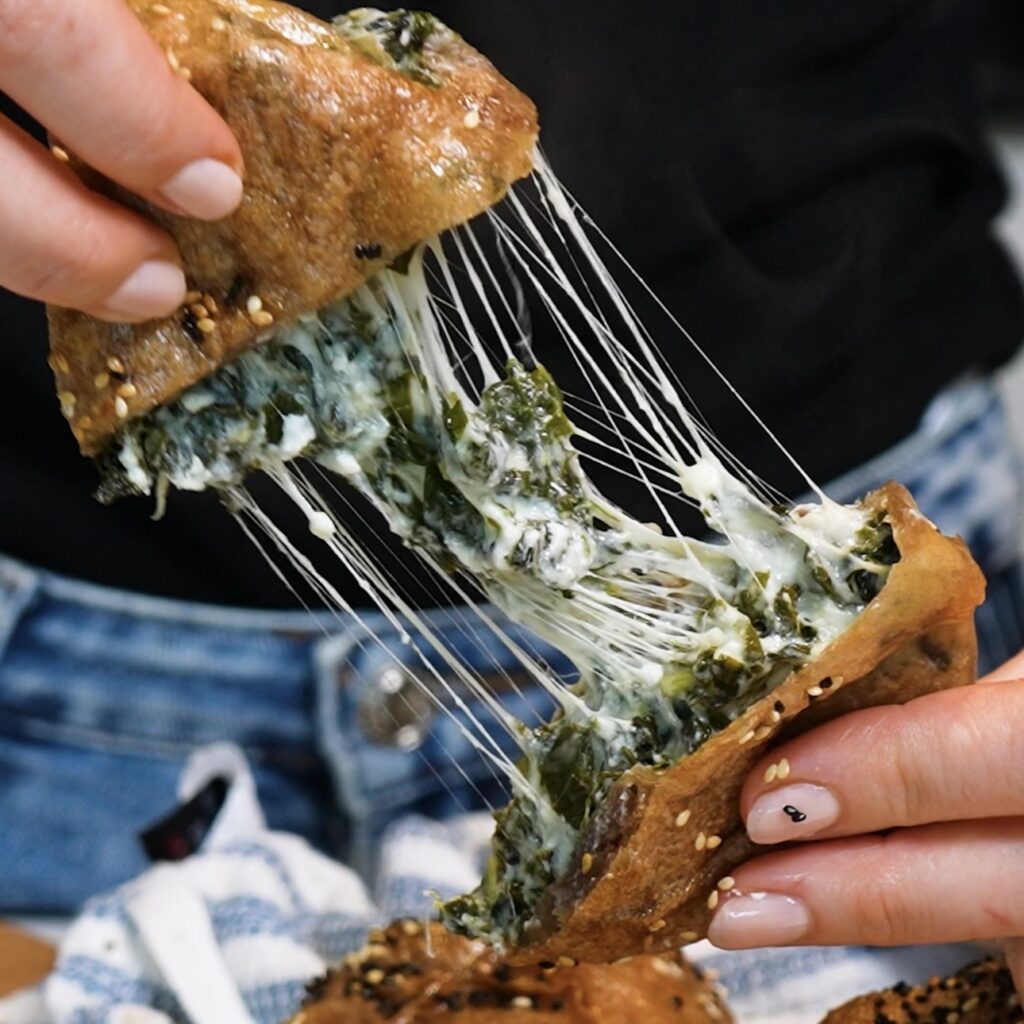 Hands tearing apart a Spinach Feta Rice Paper Bomb to reveal the melted cheese pull.