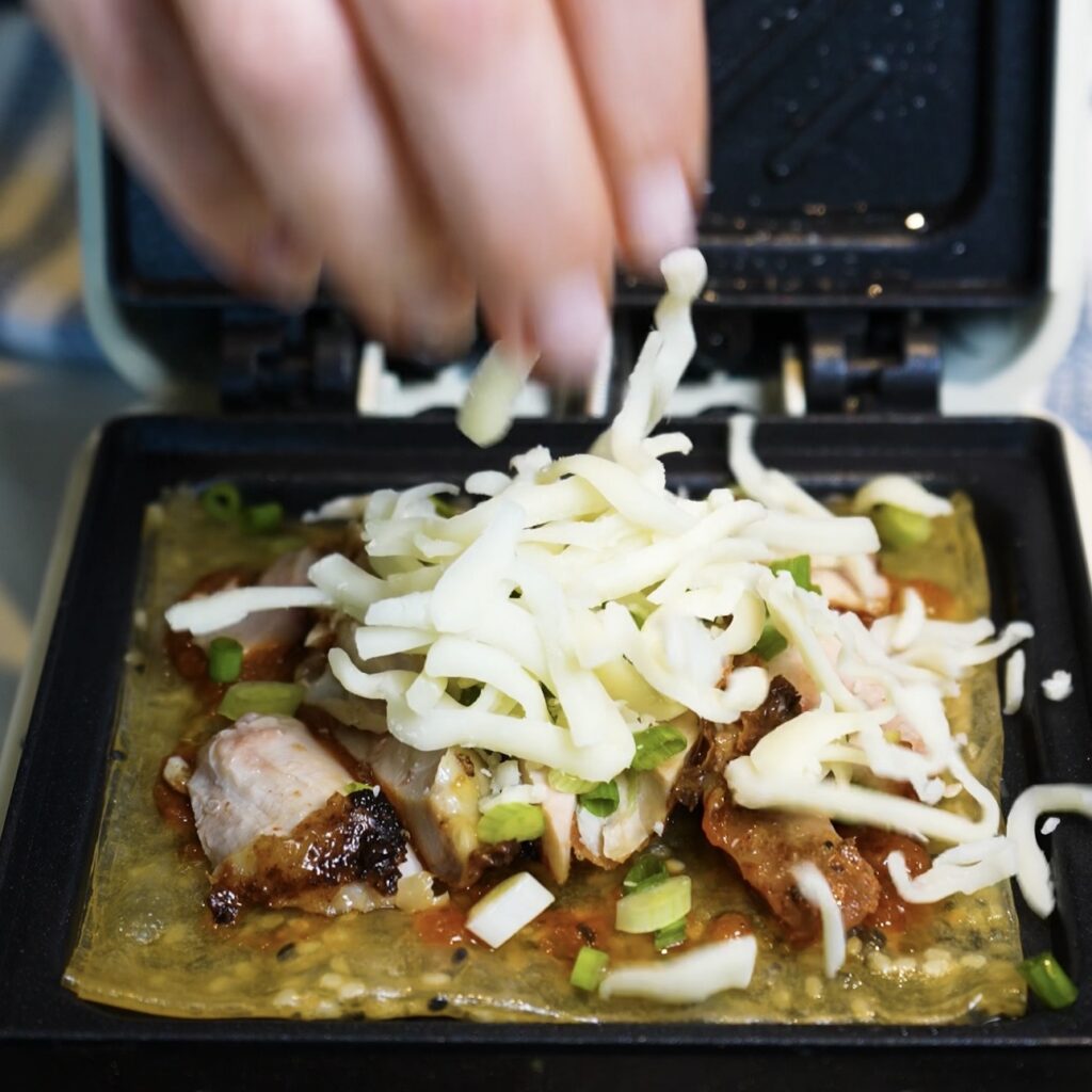 Adding shredded mozzarella over the chicken, pesto and spring onion filling for Crispy Rice Paper Toast.