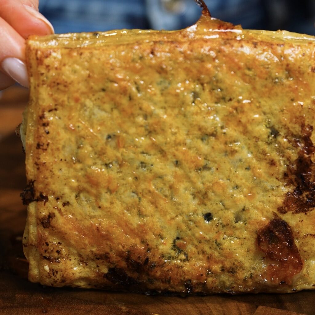 Hands holding a golden Crispy Rice Paper Toast filled with chicken, pesto and melted mozzarella.