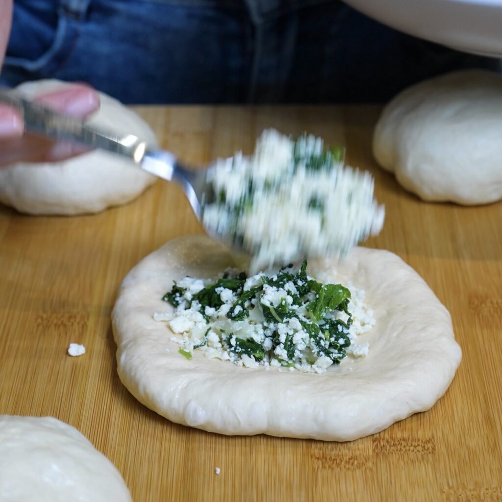 Spinach, feta and mozzarella filling being added to the centre of flattened flatbread dough.