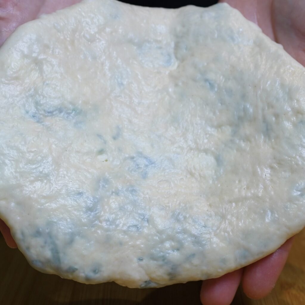 Stuffed spinach and feta flatbread dough flattened into a round before cooking.