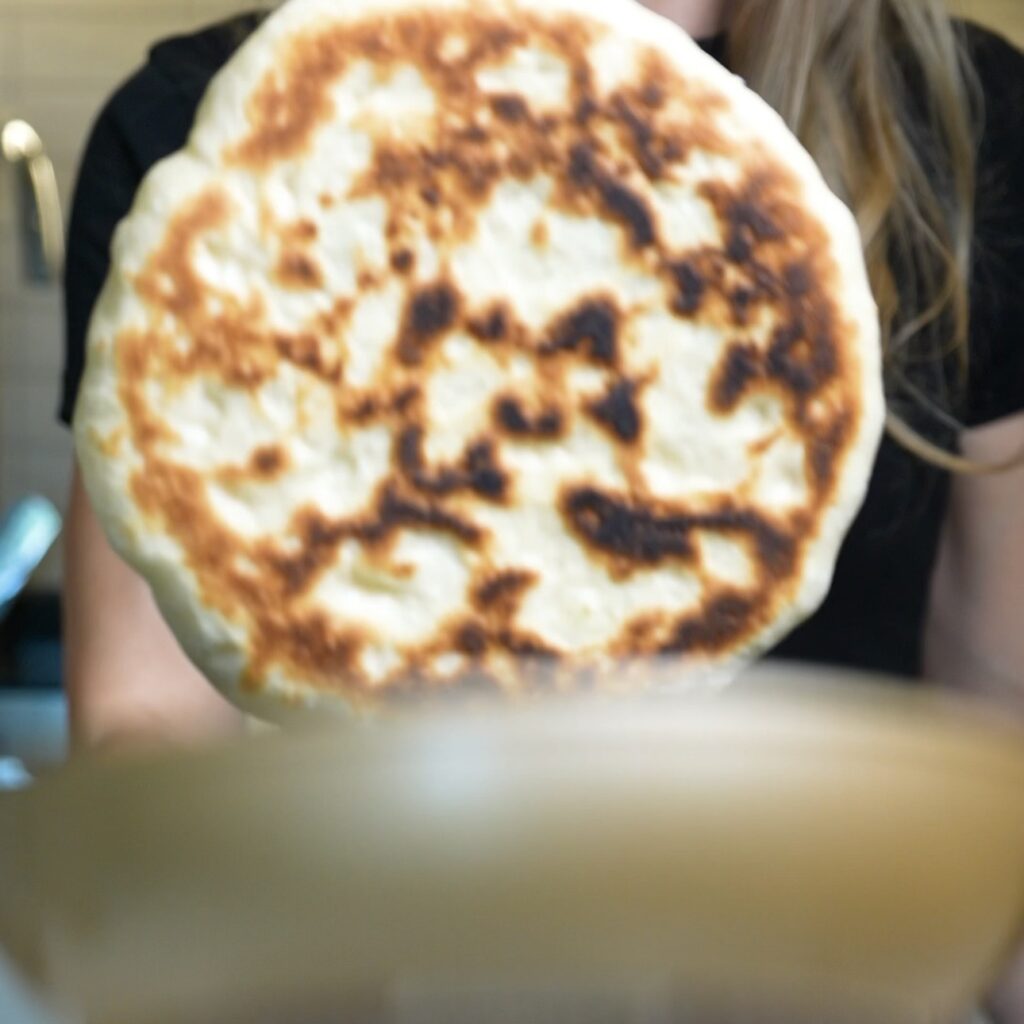 Spinach and feta flatbread being flipped in a frying pan while cooking.