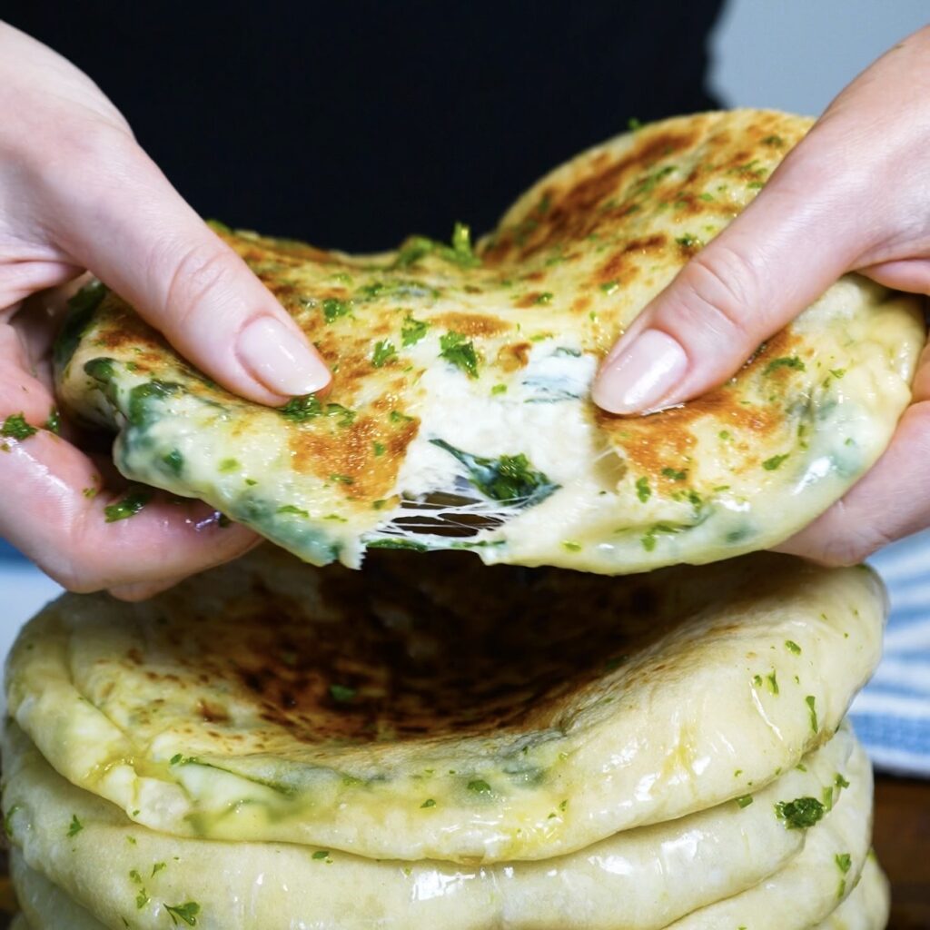 Hands tearing open a warm Spinach and Feta Flatbread to reveal the cheesy filling inside.