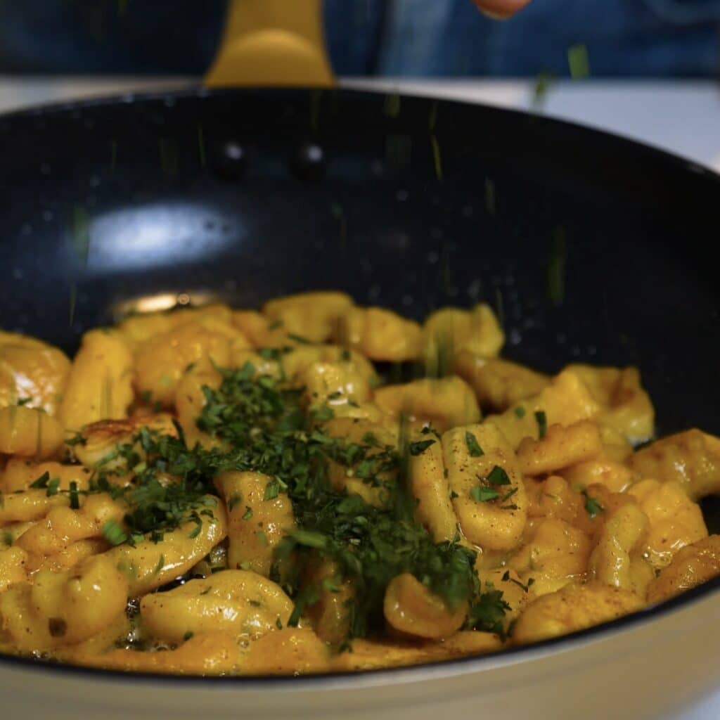 Adding chopped fresh tarragon to garlic butter sweet potato gnocchi in a frying pan