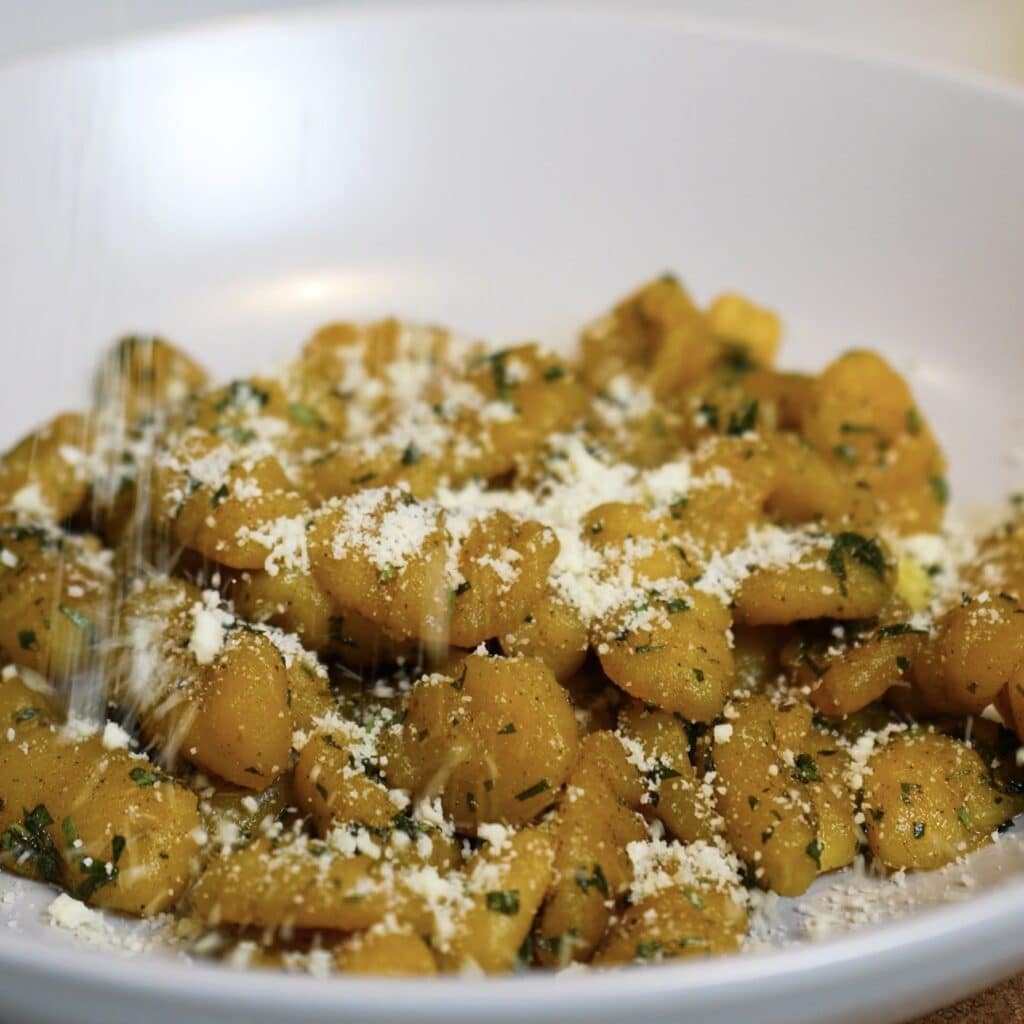 Sprinkling grated Parmesan over garlic butter sweet potato gnocchi