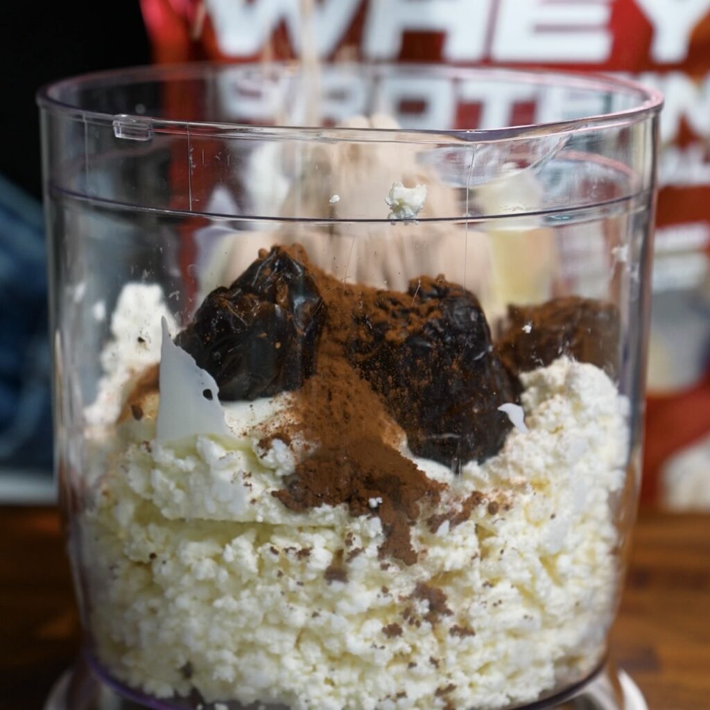 Cottage cheese, Greek-style yogurt, dates, cocoa powder and protein powder in a food processor before blending.