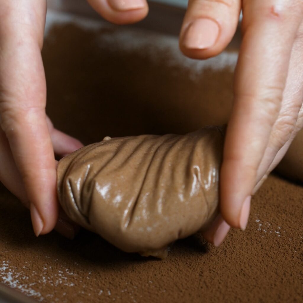 Shaped chocolate rice paper mochi placed seam-side down on a cocoa-dusted baking tray.